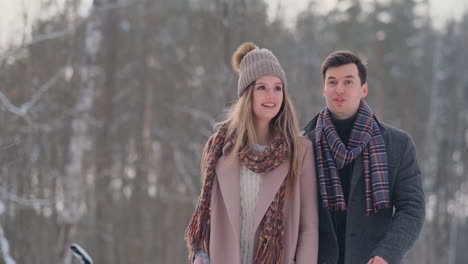 in the winter snowy forest, young men and women dressed in coats and scarves are walking and having fun. loving couple spend together valentines day.