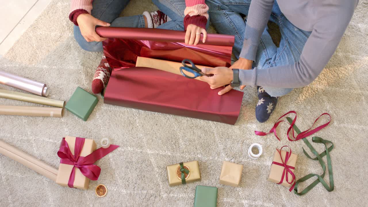 Dopo aver srotolato la carta rossa a casa, una coppia impacchetta un regalo per le feste, tagliando l'eccesso e incollando i lembi