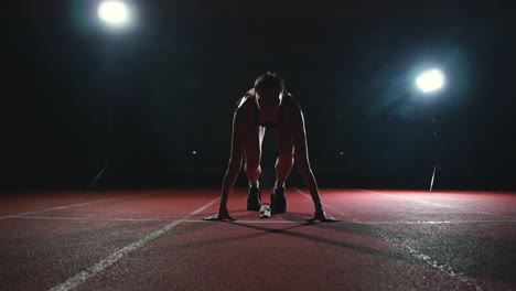 slender young girl athlete is in position to start running in the pads on the track in slow motion