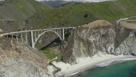 el famoso puente bixby creek de california, las olas rompiendo en la playa debajo, las montañas al fondo