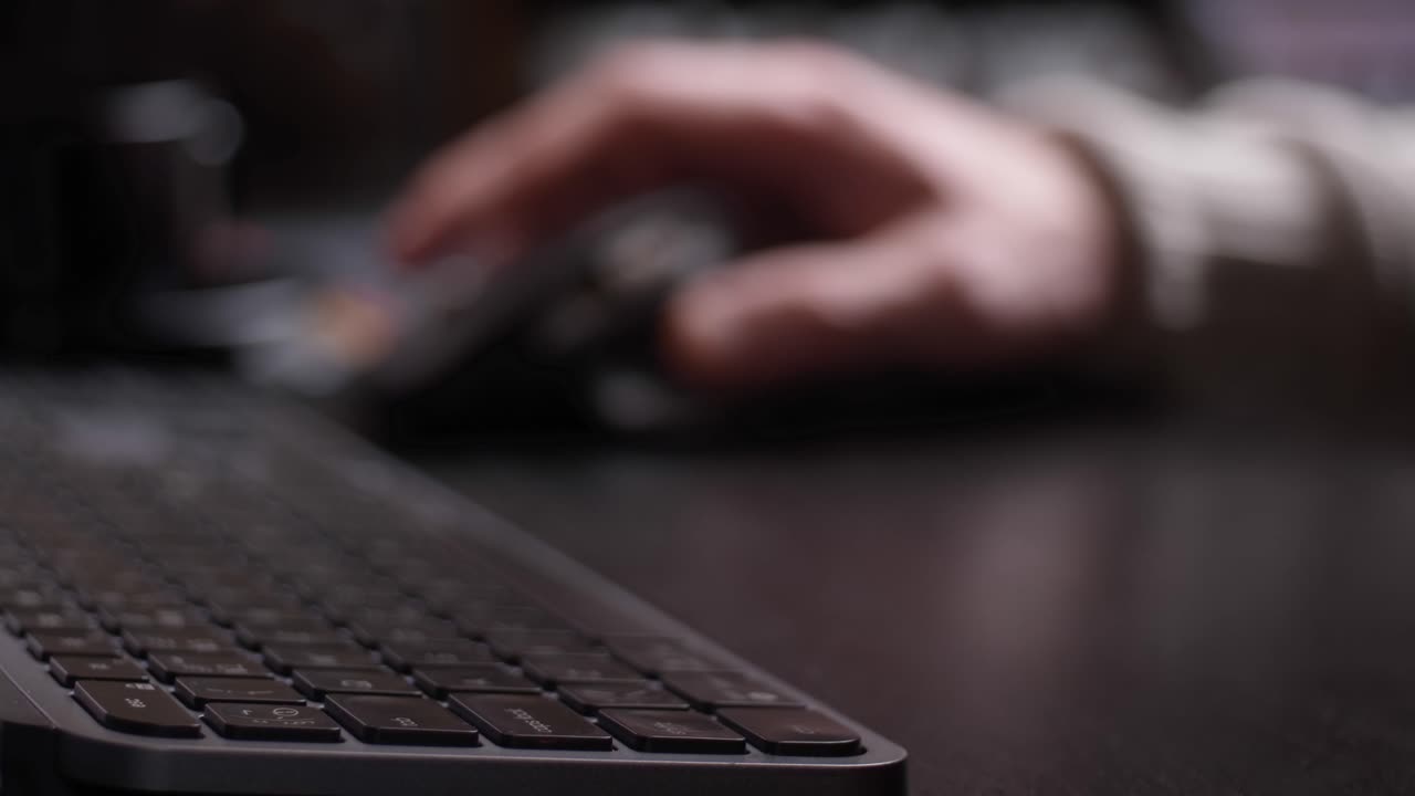 Hand working with mouse, keyboard from a side perspective with blurred background.