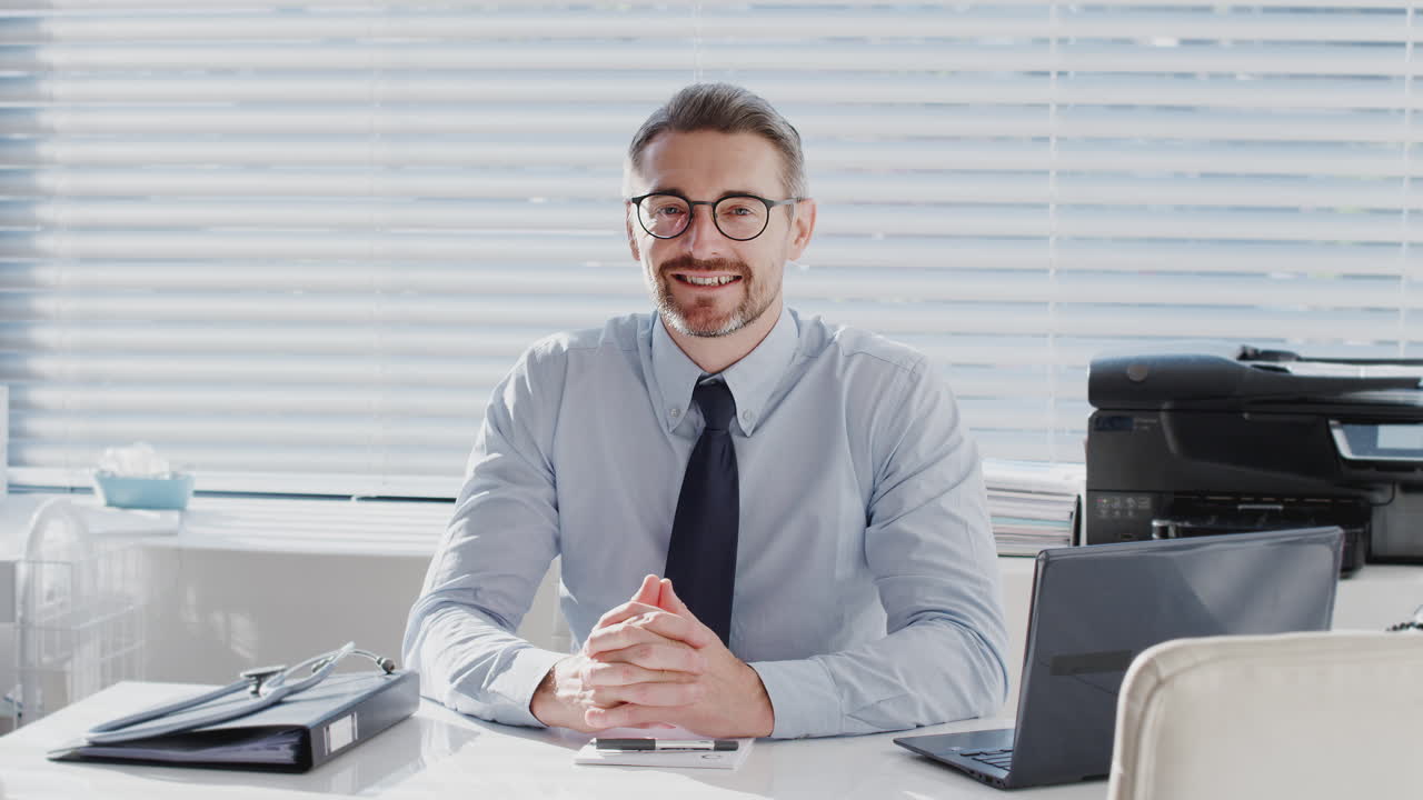 Porträt eines reifen männlichen Arztes, der hinter dem Schreibtisch im Büro sitzt