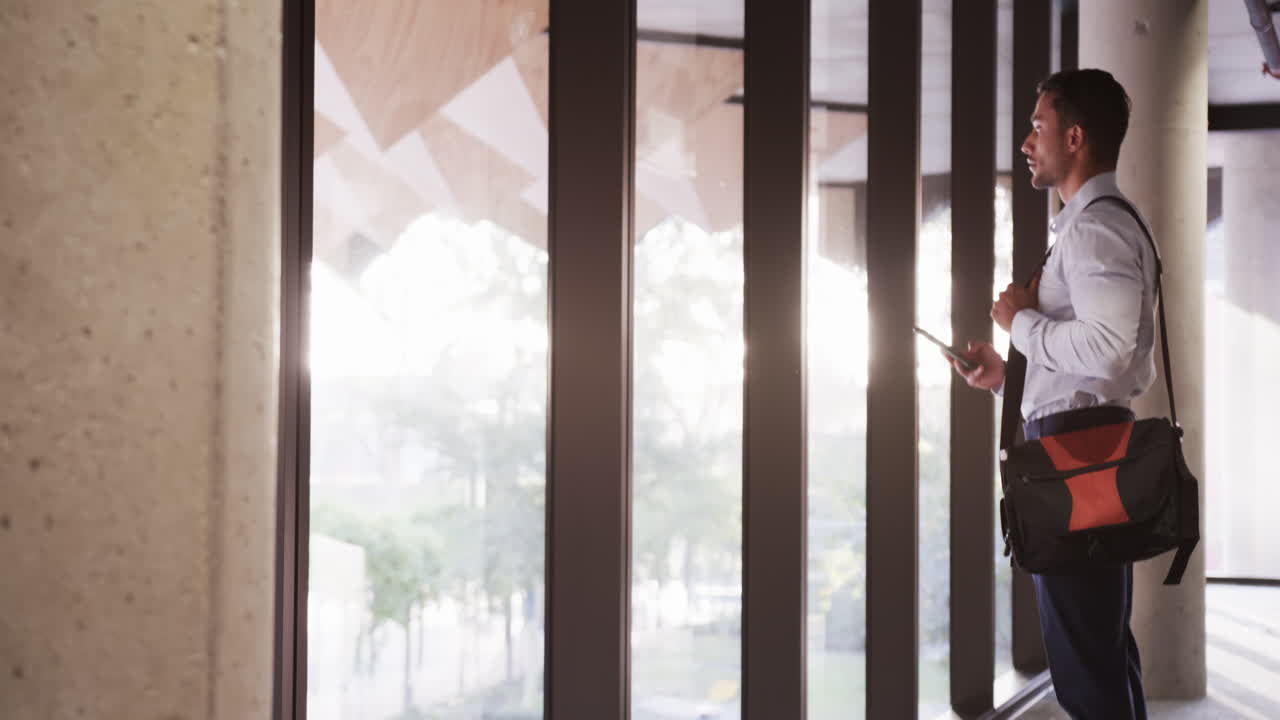 Business professional holding tablet and carrying bag, standing by office windows, copy space