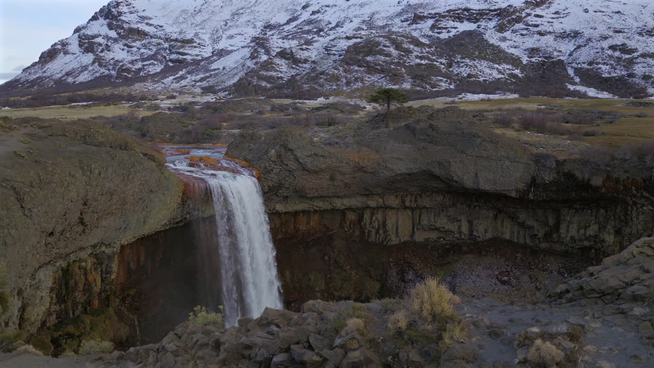 Beautiful panoramic aerial fly around the touristic attraction Salto del Agrio waterfall with snowy mountains nearby, Neuquén, Argentina