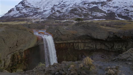 beautiful panoramic aerial fly around the touristic attraction salto del agrio waterfall with snowy mountains nearby, neuquén, argentina