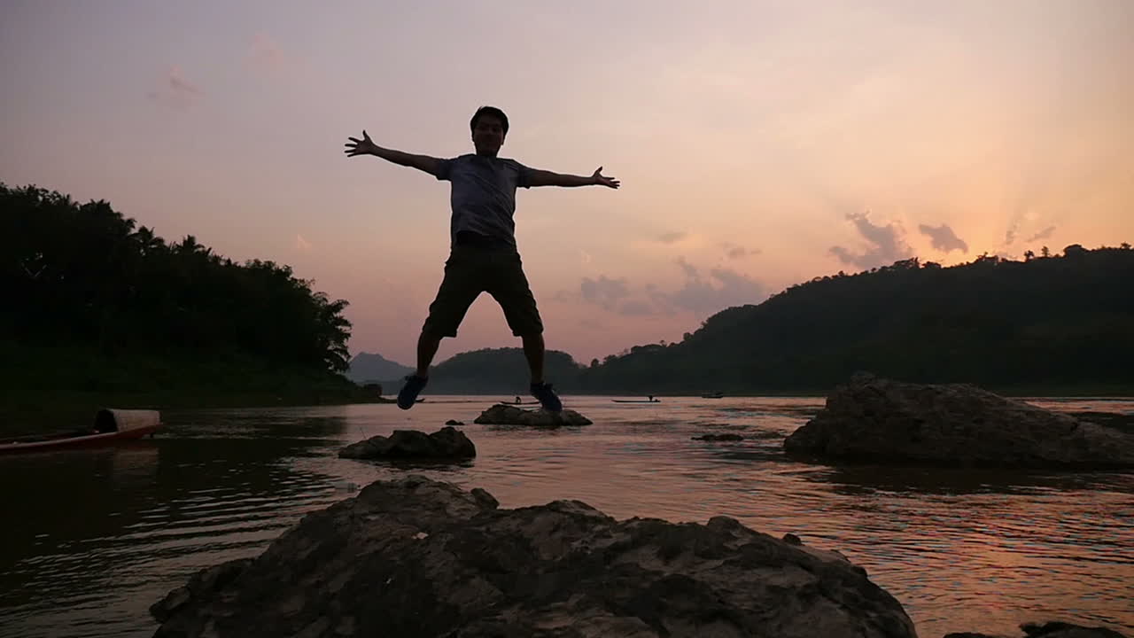 Man Standing on Rocks at Sunset by River