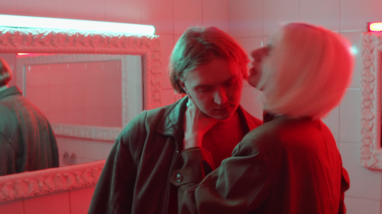 감각적인 여자가 빨간 빛으로 방에서 남자친구를 키스하고 있습니다.