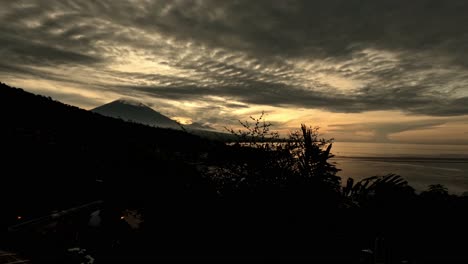 Timelapse-of-moving-cumulus-clouds-at-sunset-with-Mount-Agung-in-the-background-with-orange-sunset-and-ocean-reflection-from-Amed,-Bali,-Indonesia