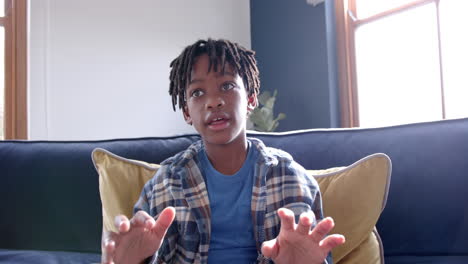 african american boy sitting on sofa having video call at home, slow motion