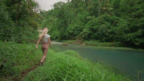 sportive woman arriving at tropical celeste river in green jungle, splashing water on face