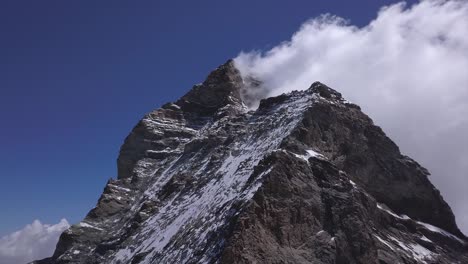 Ascending-aerial-view-of-the-jagged-peak-of-The-Matterhorn,-a-mountain-of-the-Alps,-straddling-the-border-between-Switzerland-and-Italy