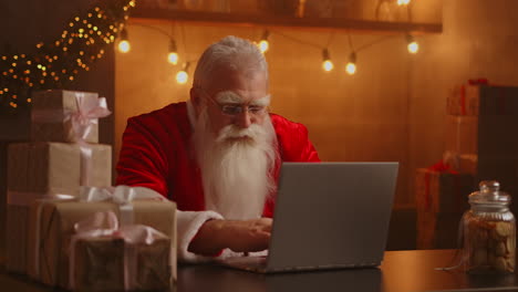 Weihnachtsmann-Benutzt-Laptop-Im-Wohnzimmer.-Porträt-Des-Nachdenklichen-Weihnachtsmanns,-Der-Mit-Modernem-Laptop-In-Dekoriertem-Haus-Tippt.-Hochwertiges-4K-Filmmaterial