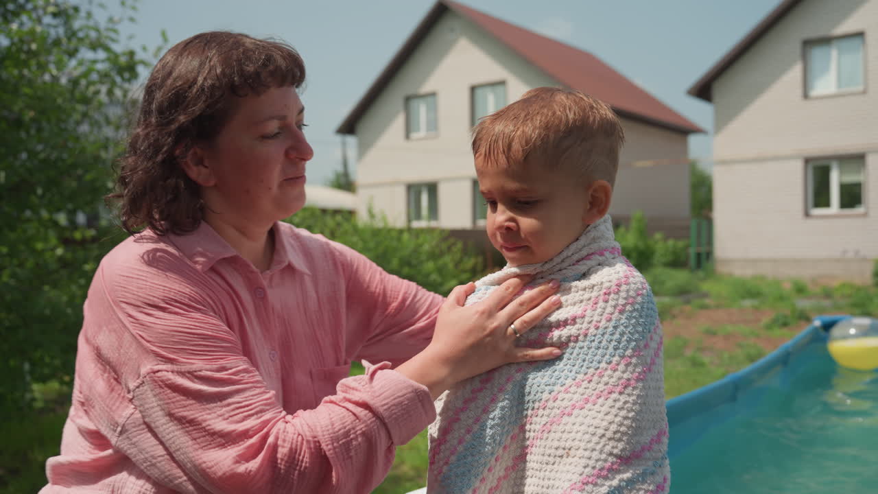 Loving Mother Embraces Young Boy By Poolside, Gentle Mother Holds Small Child After Swimming In Backyard, Affectionate Mother Wraps Her Young Son In Towel Beside Pool During Warm Afternoon