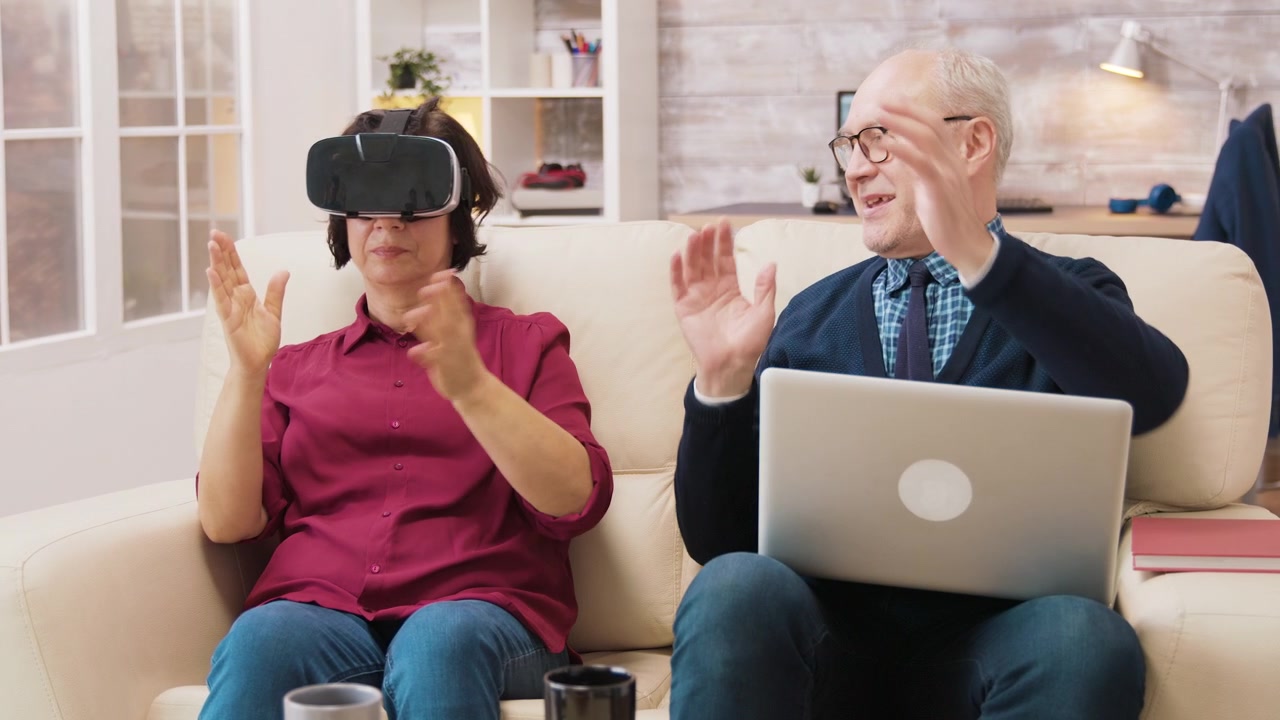 Coppia anziana che usa visore per realtà virtuale e laptop a casa
