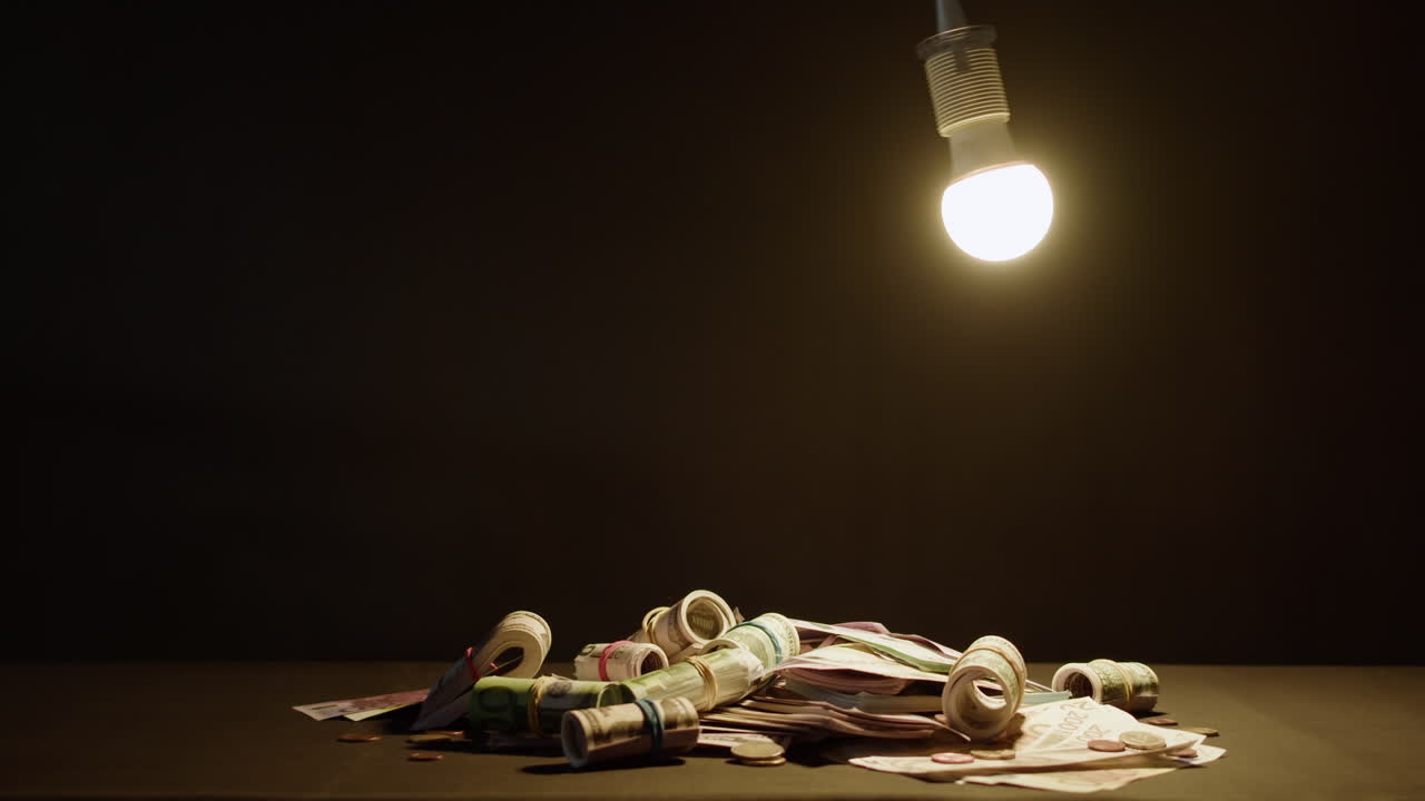 Pila di banconote arrotolate e monete sotto una lampadina luminosa
