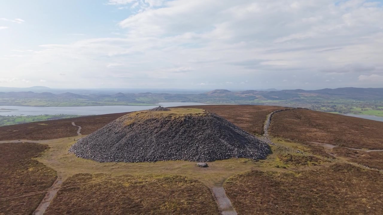 Luftfoto cirkler omkring en gammel stenkæmpehøj på toppen af Knocknarea-bakken med udsigt til fjerne søer.