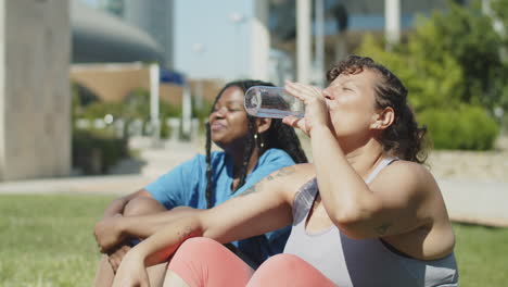 Side view of satisfied women finished workout, sitting on lawn