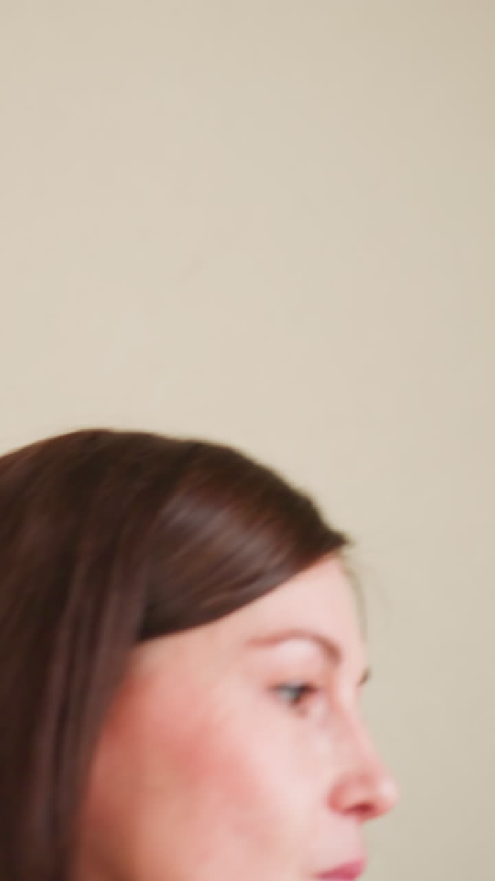 Profile view of businesswoman with auburn hair in gray blazer standing in office hallway. Professional female looking toward corridor with doors visible in background. Corporate setting with cream walls