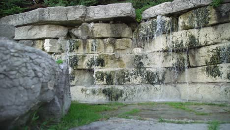 Toma-Panorámica-Baja-De-Una-Cascada-En-Un-Jardín-Con-Un-Muro-De-Piedra-Decorativo.