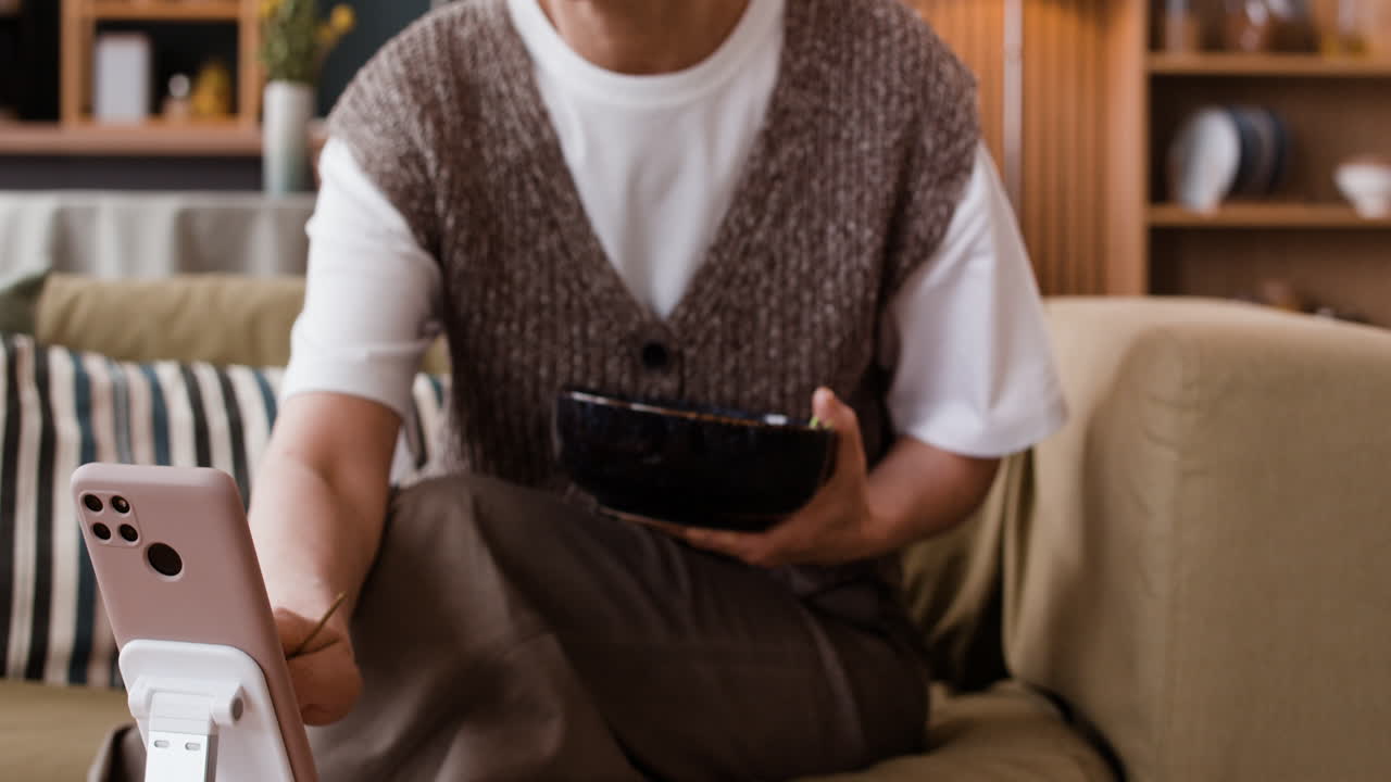 Woman eating a meal and using her smartphone on the couch at home