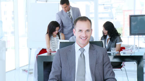 Smiling-manager-with-his-team-working-in-the-background