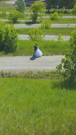 happy newly wedded couple in green terraced park against pavilion and large river on warm summer day aerial backside view