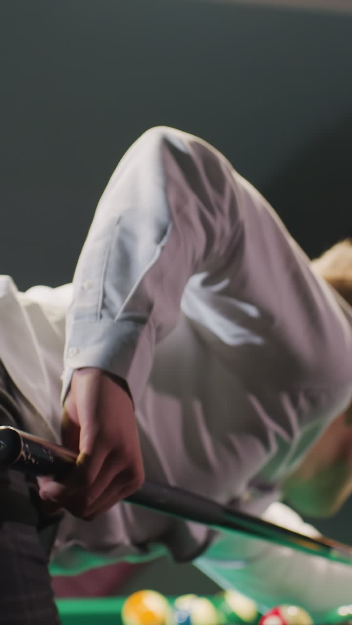 primer plano de fondo del jugador de billar con camisa blanca y pantalones grises inclinado sobre la mesa de billar verde, agarrando el palo de la clave con precisión. la iluminación aérea arroja un brillo cálido mientras se alinea en el tiro estratégico