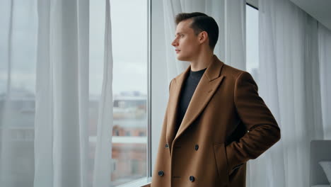 thoughtful man in brown coat looks out window