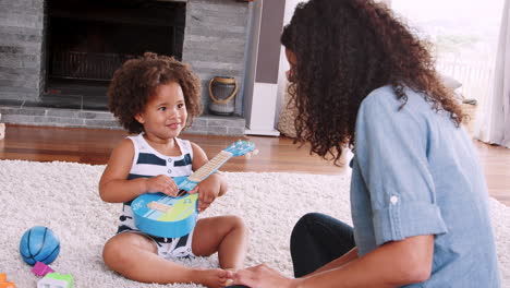 una joven negra tocando el ukulele con su madre en la sala de estar