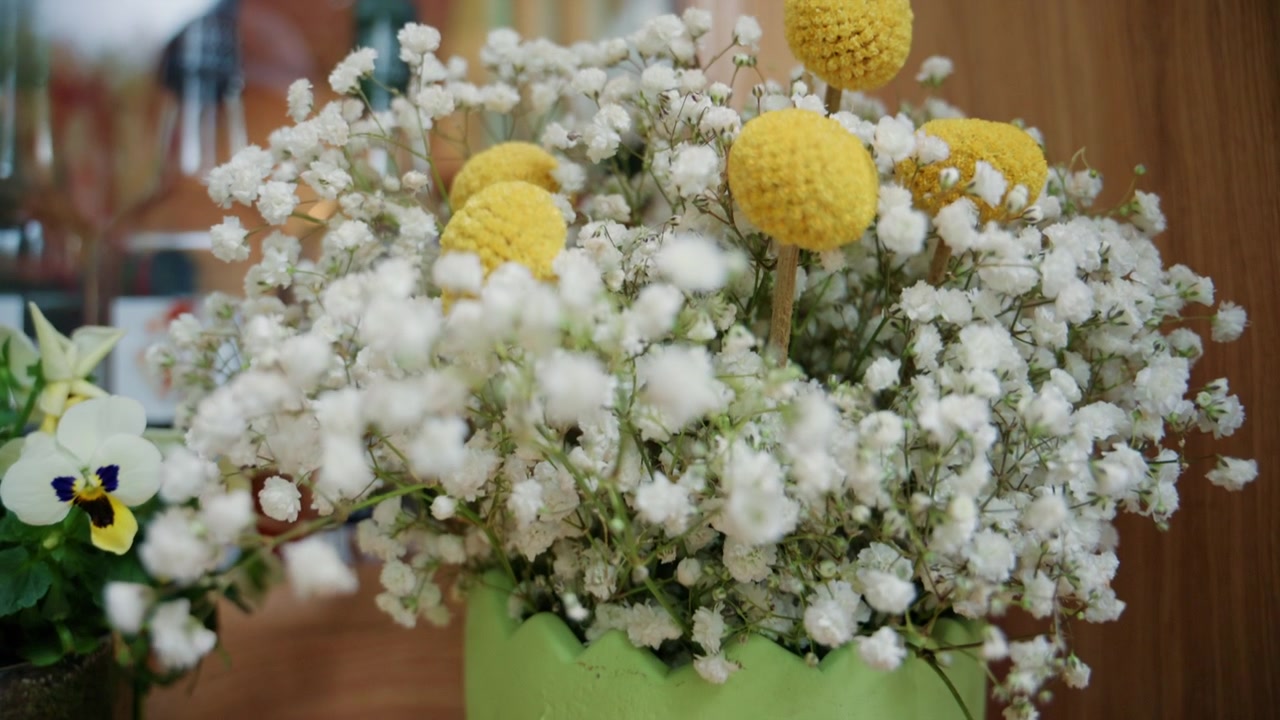 Close up of a floral arrangement featuring delicate white blossoms and yellow flowers in a decorative vase