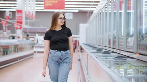 young lady standing in front of display at well-lit mall, looking at display and placing her hand on it, reflecting the ambiance of modern shopping experience