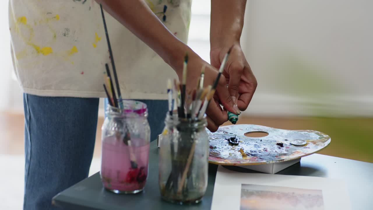 African American woman seeing print picking tube, squeezing onto palette loading brush at studio