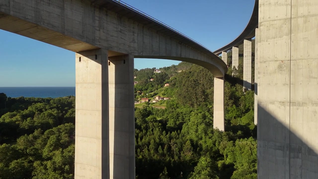 Vista aerea con drone accanto a un alto viadotto in cemento che attraversa una valle boscosa. Ponte.