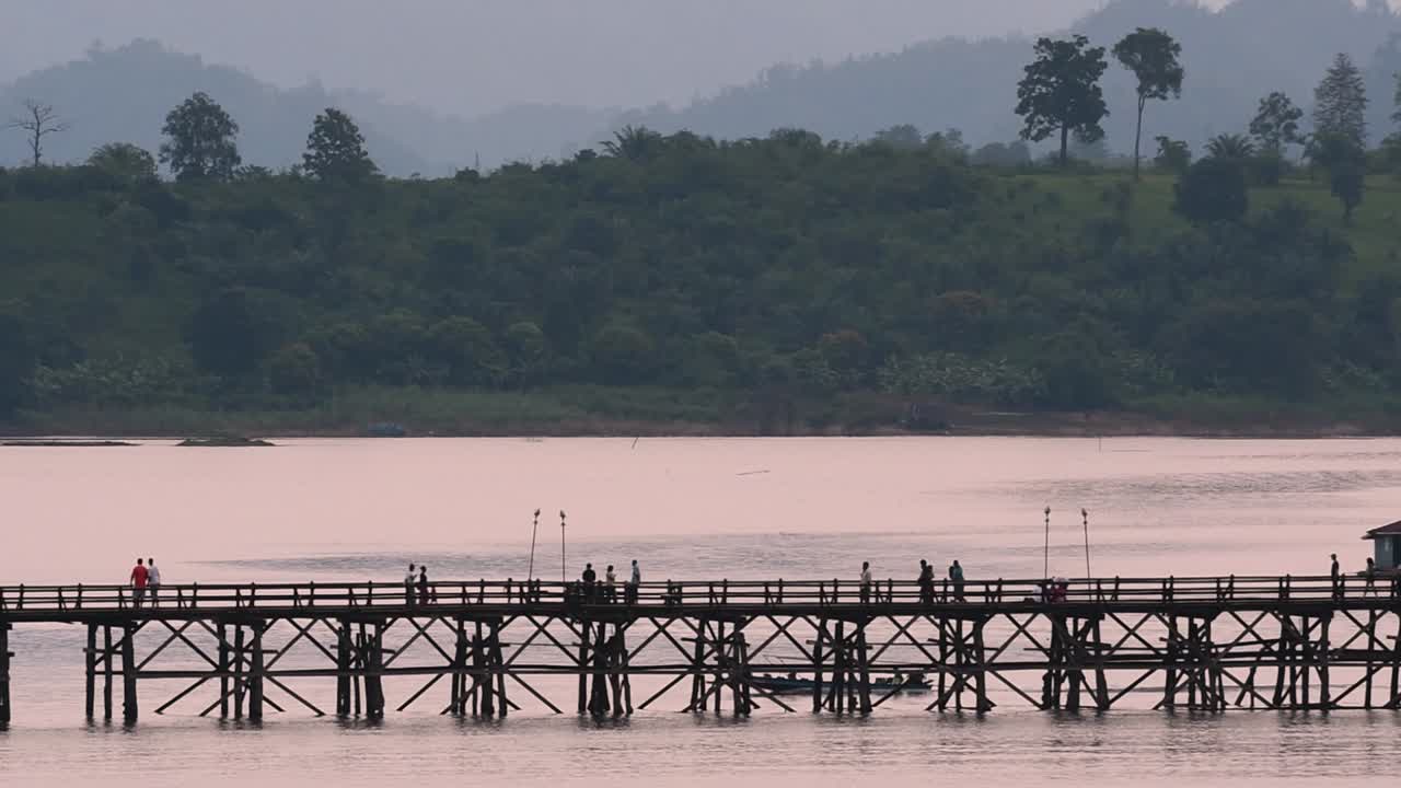 mon bridge y una lancha siguieron a toda velocidad detrás de la estructura mientras la gente caminaba por el puente, dibujando siluetas mientras oscurecía, en cámara lenta