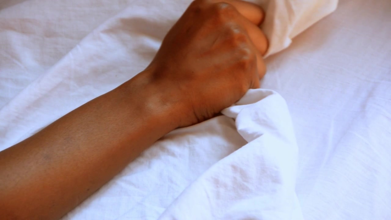 Mano di donna di colore che afferra e tira via lenzuola bianche.