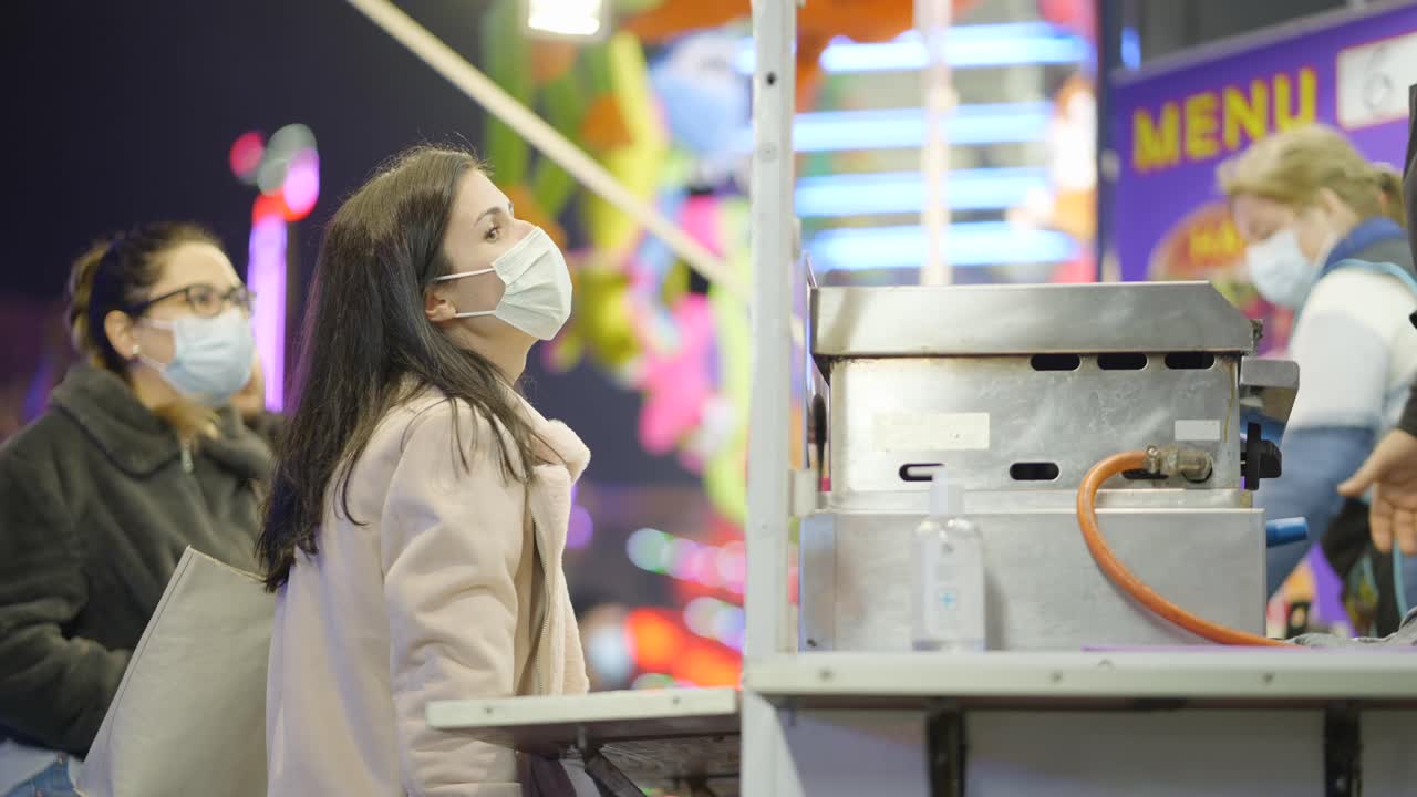 People waiting in line at a food stall at a night market during a pandemic.