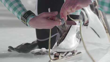 una mujer que se pone los patines de hielo en la pista de patinaje sobre hielo y se ata los cordones de los zapatos de cerca