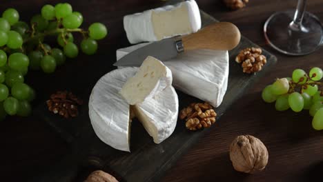 brie cheese with walnuts and grapes on a cutting board.