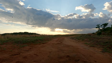la luz del sol se rompe a través de nubes dramáticas sobre un camino de tierra rodeado de campos de hierba por la mañana