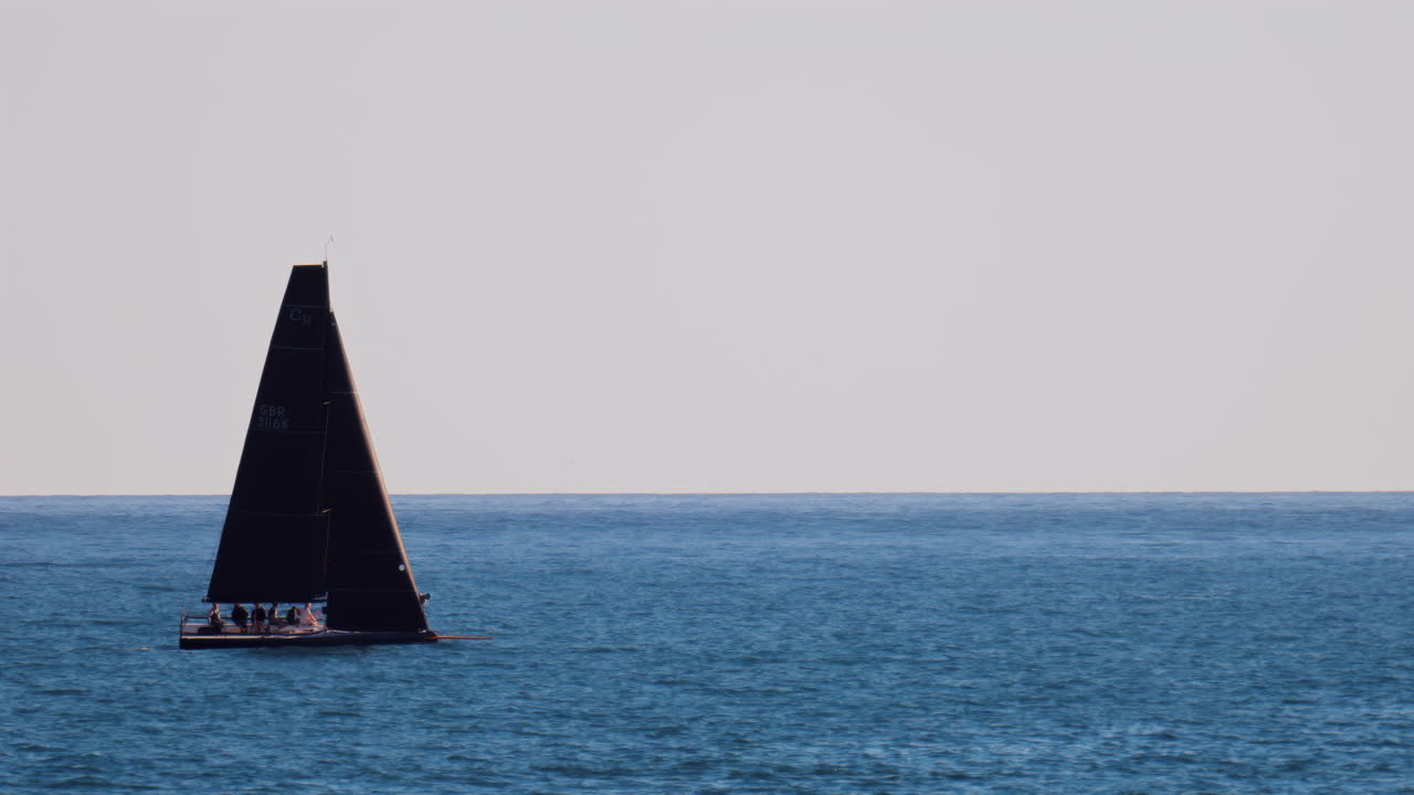 Nice, France - February 10, 2025: A black sailboat moving on the sea