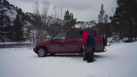 man walks toward hiking backpack next to parked suv car on snow