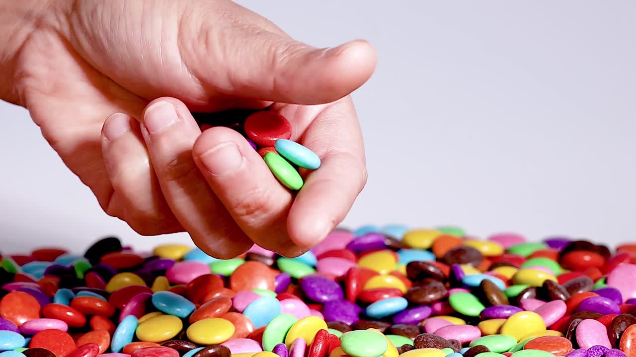 Close-up of hands picking and sorting colorful candies on a flat surface.