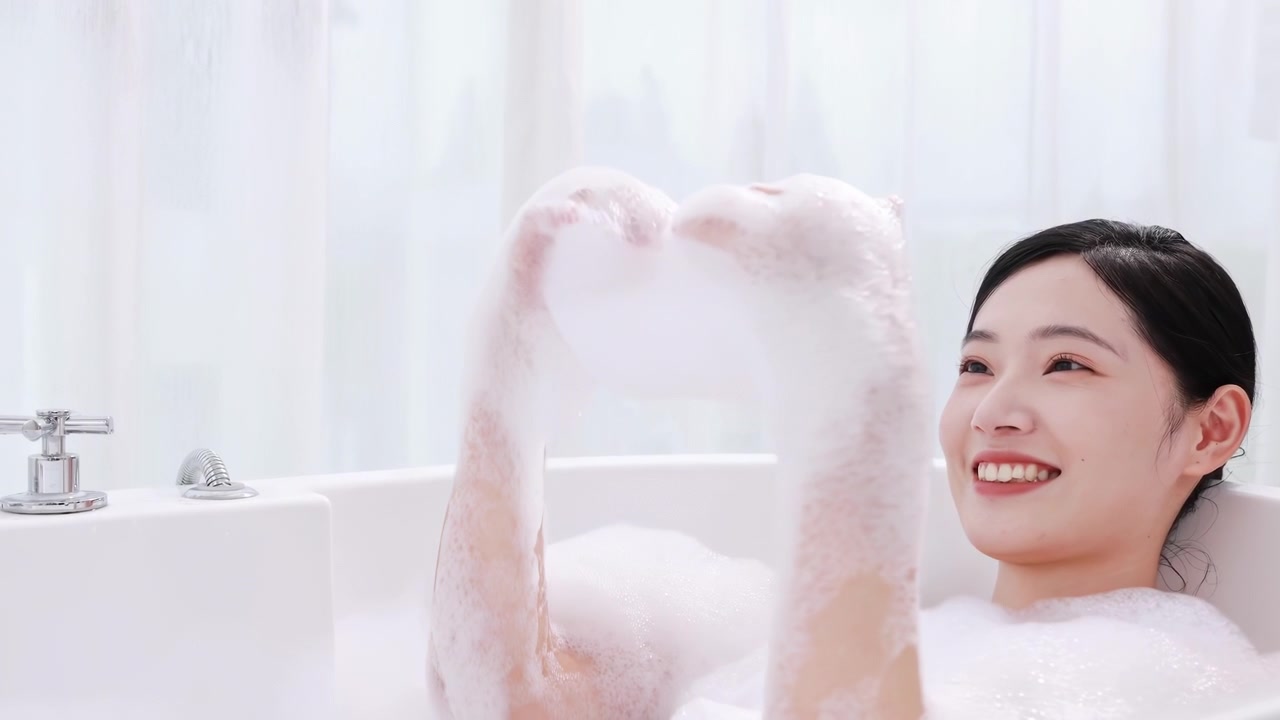 Người phụ nữ thanh lịch, quyến rũ đang thổi bọt trắng khi tắm trong phòng tắm sang trọng. Cô gái tận hưởng bồn tắm cao cấp, vui vẻ thổi bong bóng, trải nghiệm chăm sóc cơ thể thư giãn.