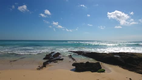 Statische-Aufnahme-Von-Bali-Beach-Mit-Blauem-Sonnigem-Himmel-Und-Ein-Paar-Flauschigen-Wolken,-Wunderschöne-Tropische-Uluwatu-küstenlinie,-Urlaubsansicht-In-Indonesien