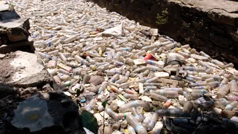 Plastic-bottle-polluting-narrow-stream-in-city,-backed-up-against-gate-preventing-pollution-reaching-the-ocean-and-causing-environmental-disaster