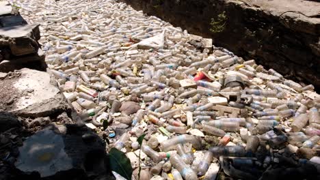 plastic bottle polluting narrow stream in city, backed up against gate preventing pollution reaching the ocean and causing environmental disaster