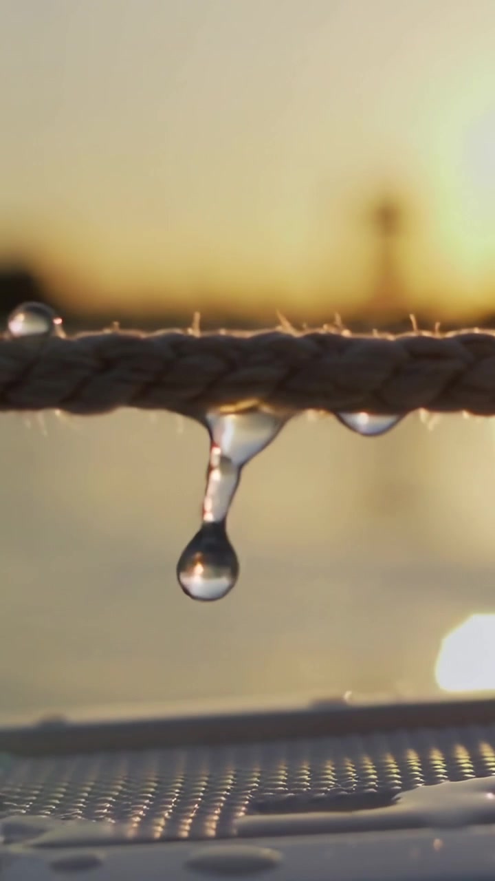 Vídeo vertical: Gotas se formando em corda se desprendendo da gravidade, caindo no convés enquanto o sol reflete na cunha.