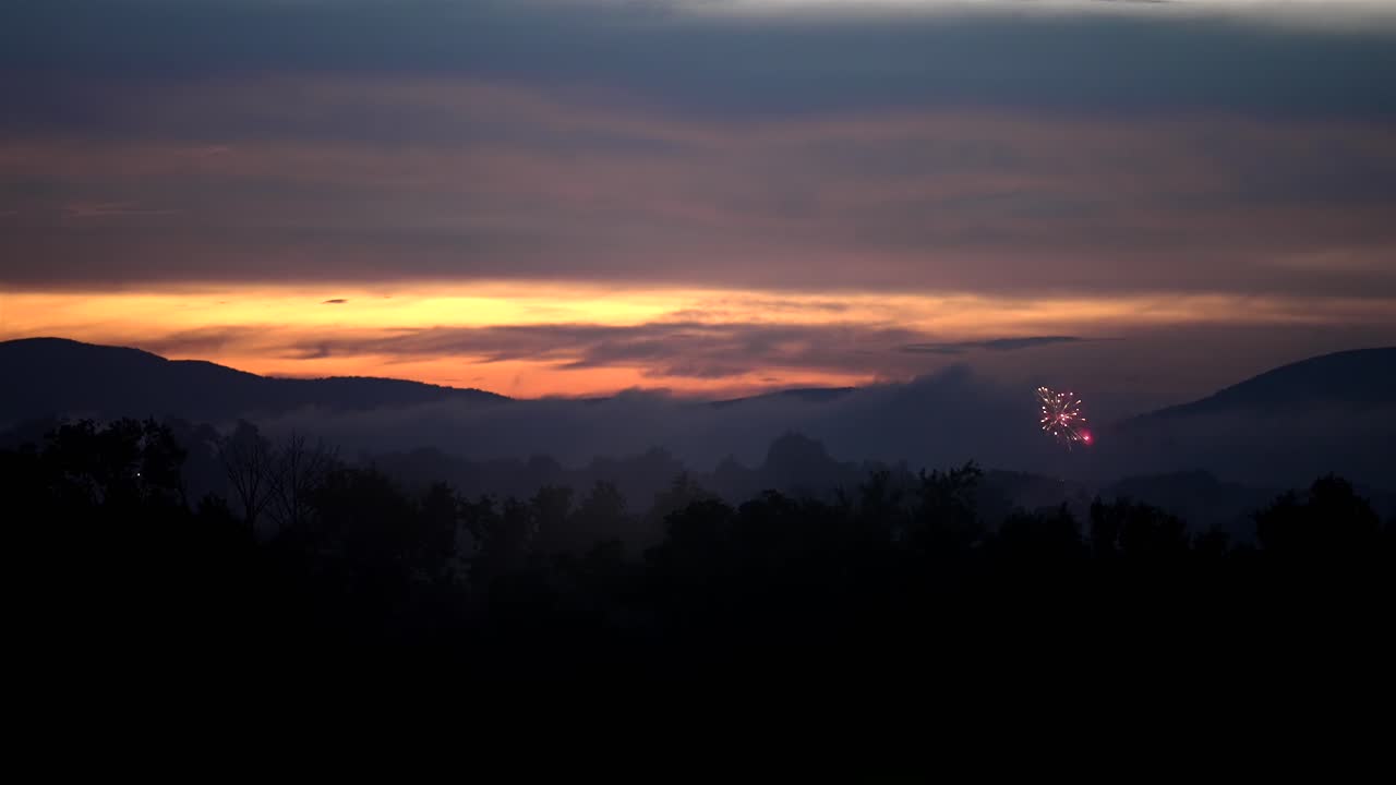 산의 실루 아래 지평선에 오렌지색 은 빛과 함께 저녁에 공중으로 발사되는 불꽃놀이의 개요