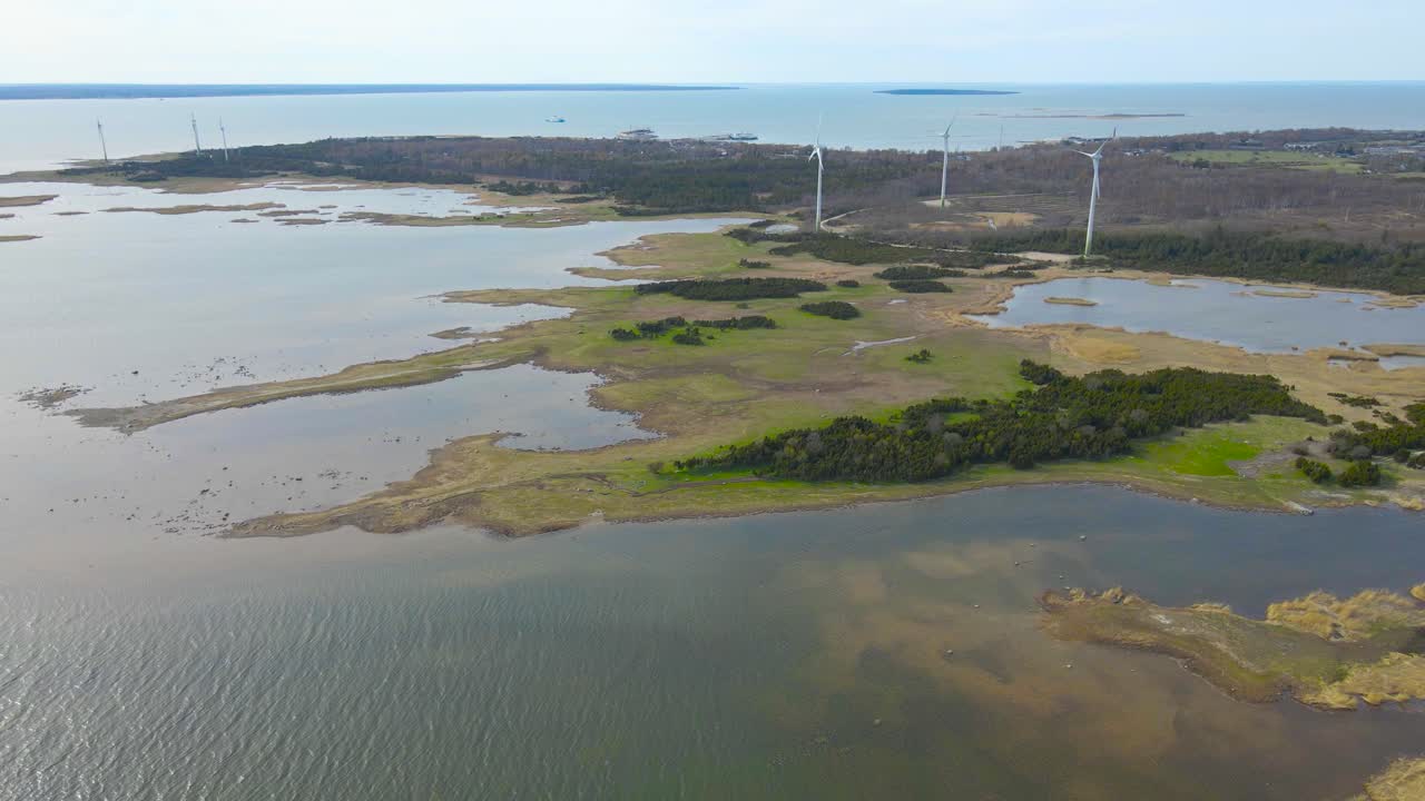 Gorgeous aerial drone footage view of a wetland oxbow lake area where large renewable energy windmills are spinning and creating energy at a sunny day. Baltic sea touching Puhtulaid land area, grassy.