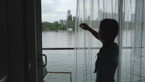 woman opening the curtain of his cruise ship room with a view of vienna city